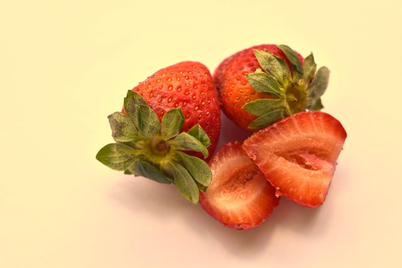 The same strawberry still life shot with the wrong white balance preset, leaving a heavy warm yellow cast across the whole frame. The neutral background has turned cream-yellow and the reds look muddied. The error is baked into the JPEG.